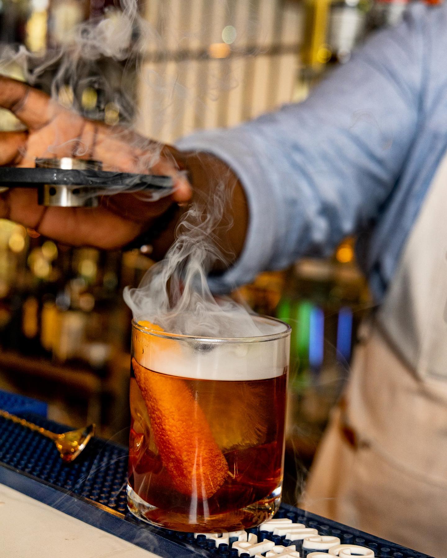 Smoked old fashioned cocktail with billowing smoke at the bar